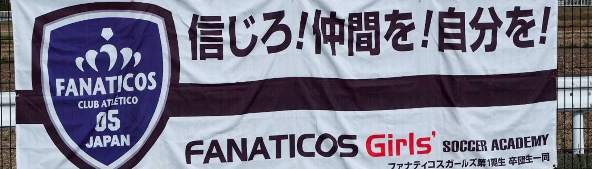 ファナティコスガールズサッカーアカデミーの横断幕。クラブロゴと「信じろ！仲間を！自分を！」のスローガン